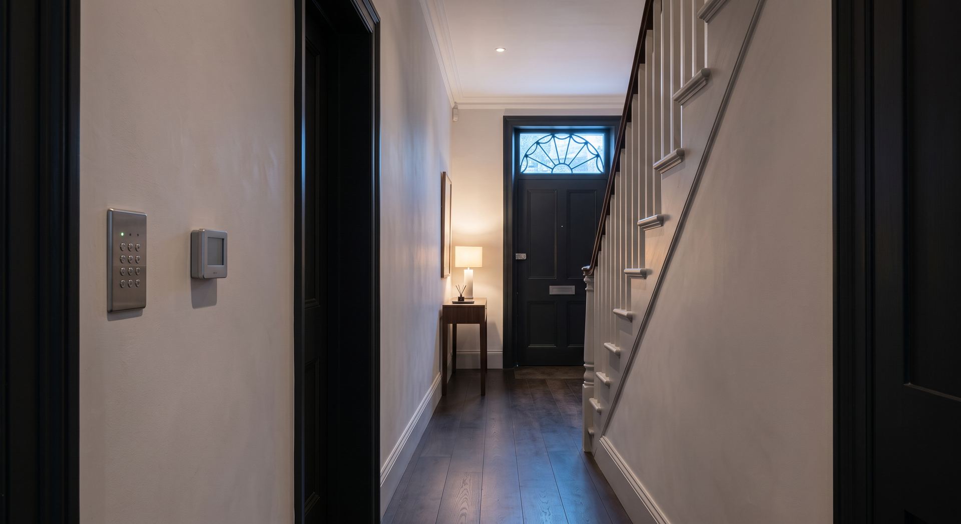 A quiet townhouse hallway at dusk with a security keypad and thermostat on the wall